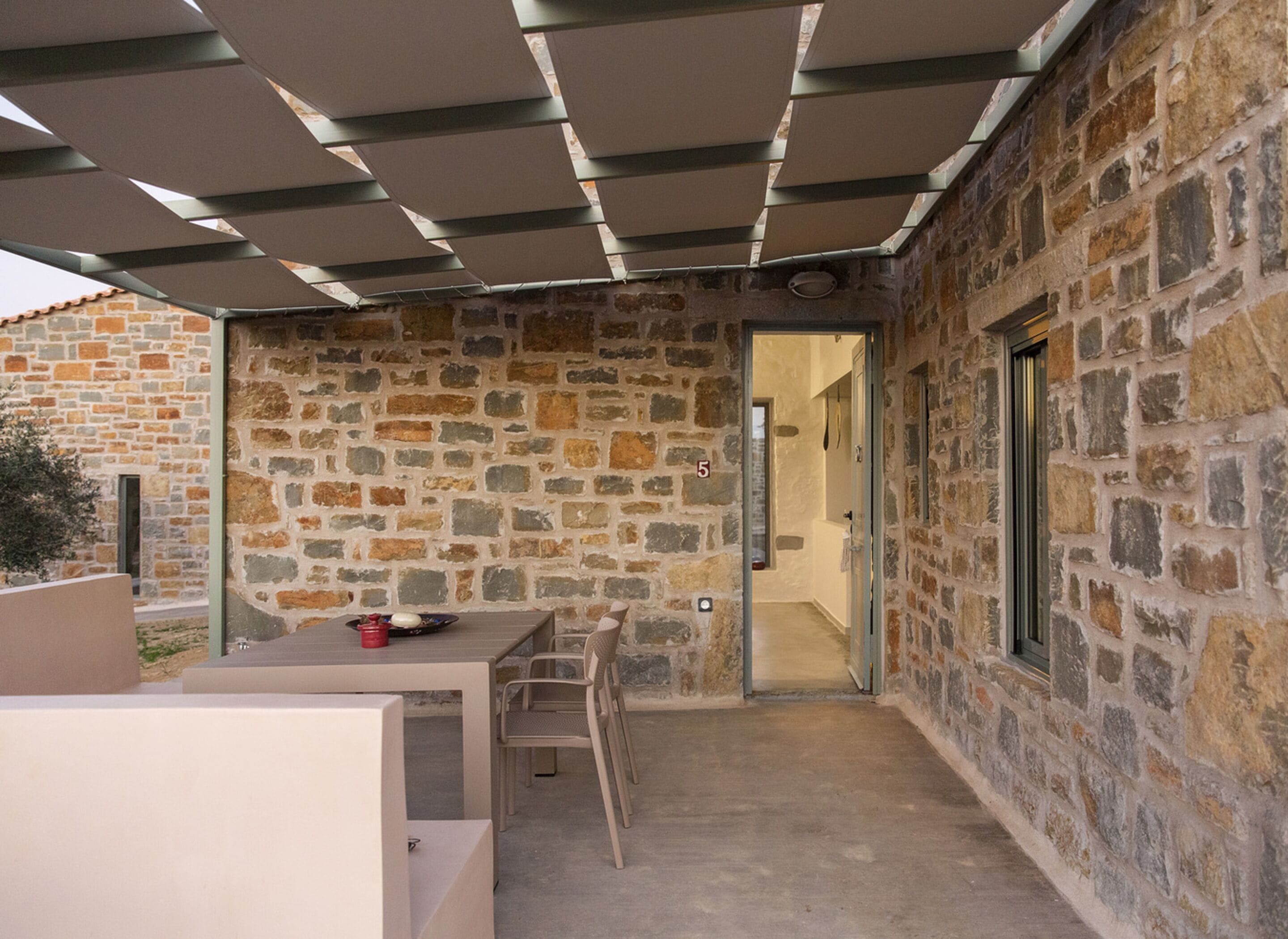 A stone-walled outdoor patio with a table and chairs, a covered seating area, and a door leading inside.