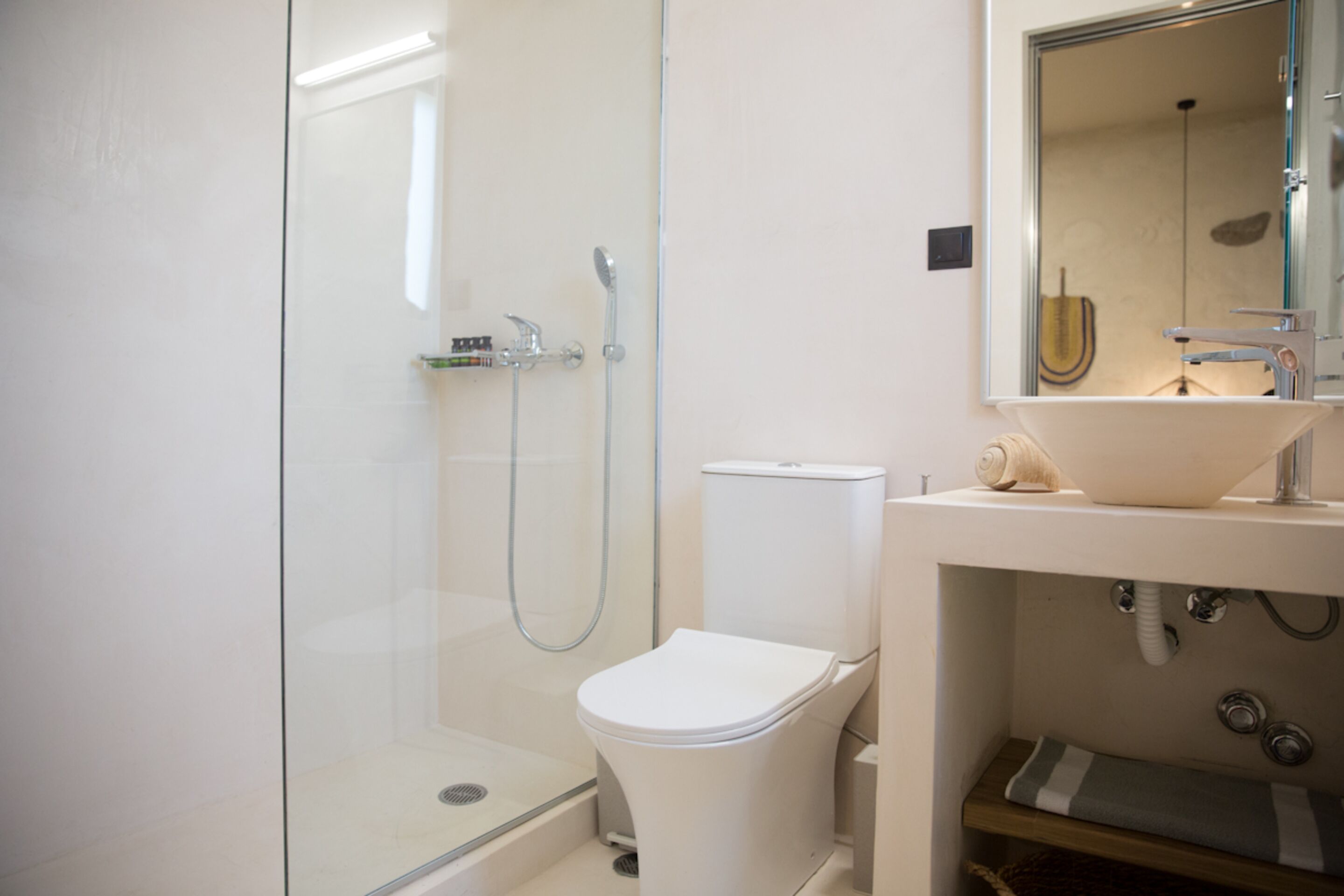 A modern bathroom with a glass-enclosed shower, a white toilet, and a sink with a mirror above it.