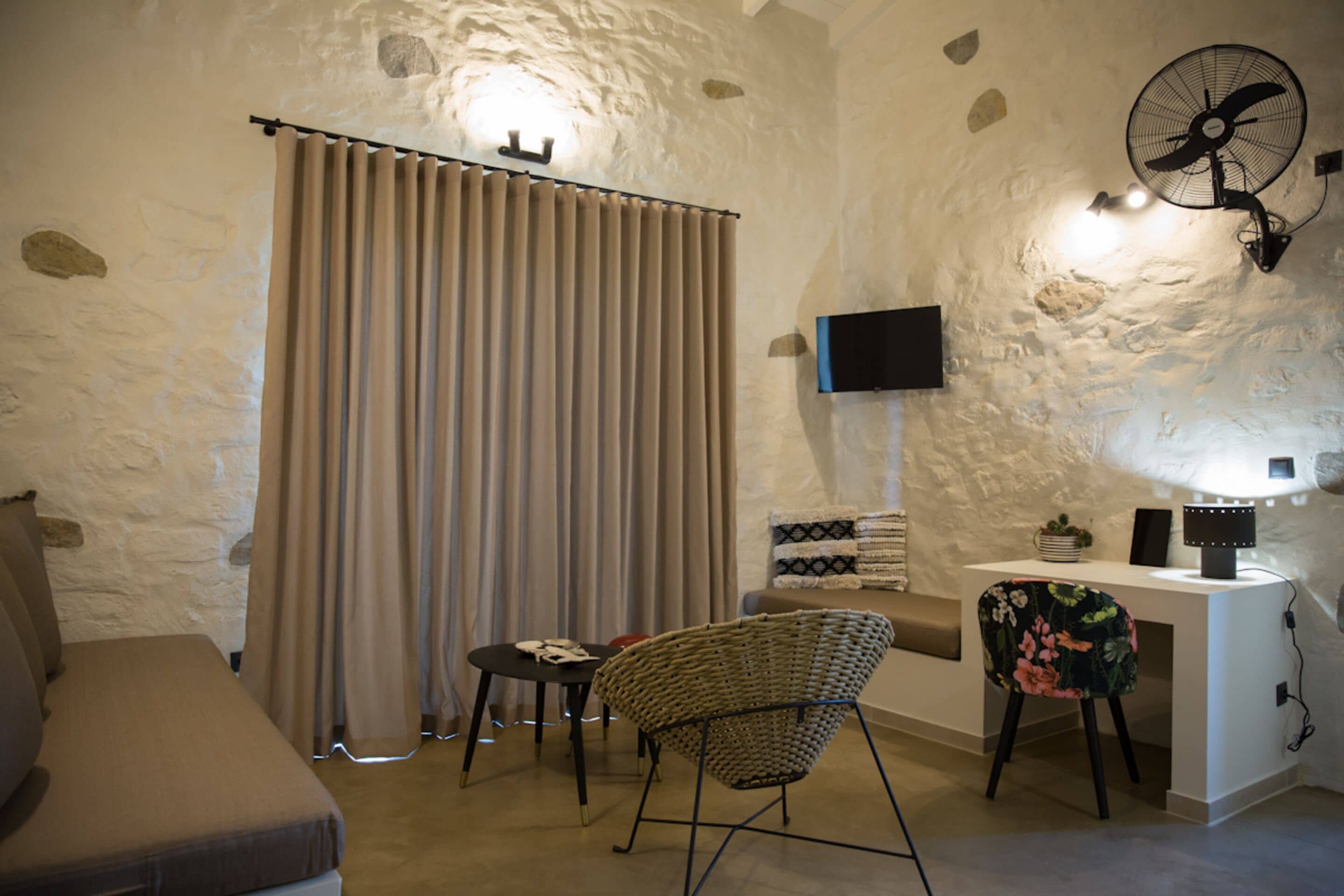 Habitació acollidora amb un sofà, una taula amb una làmpada, una cadira, un televisor i un ventilador.