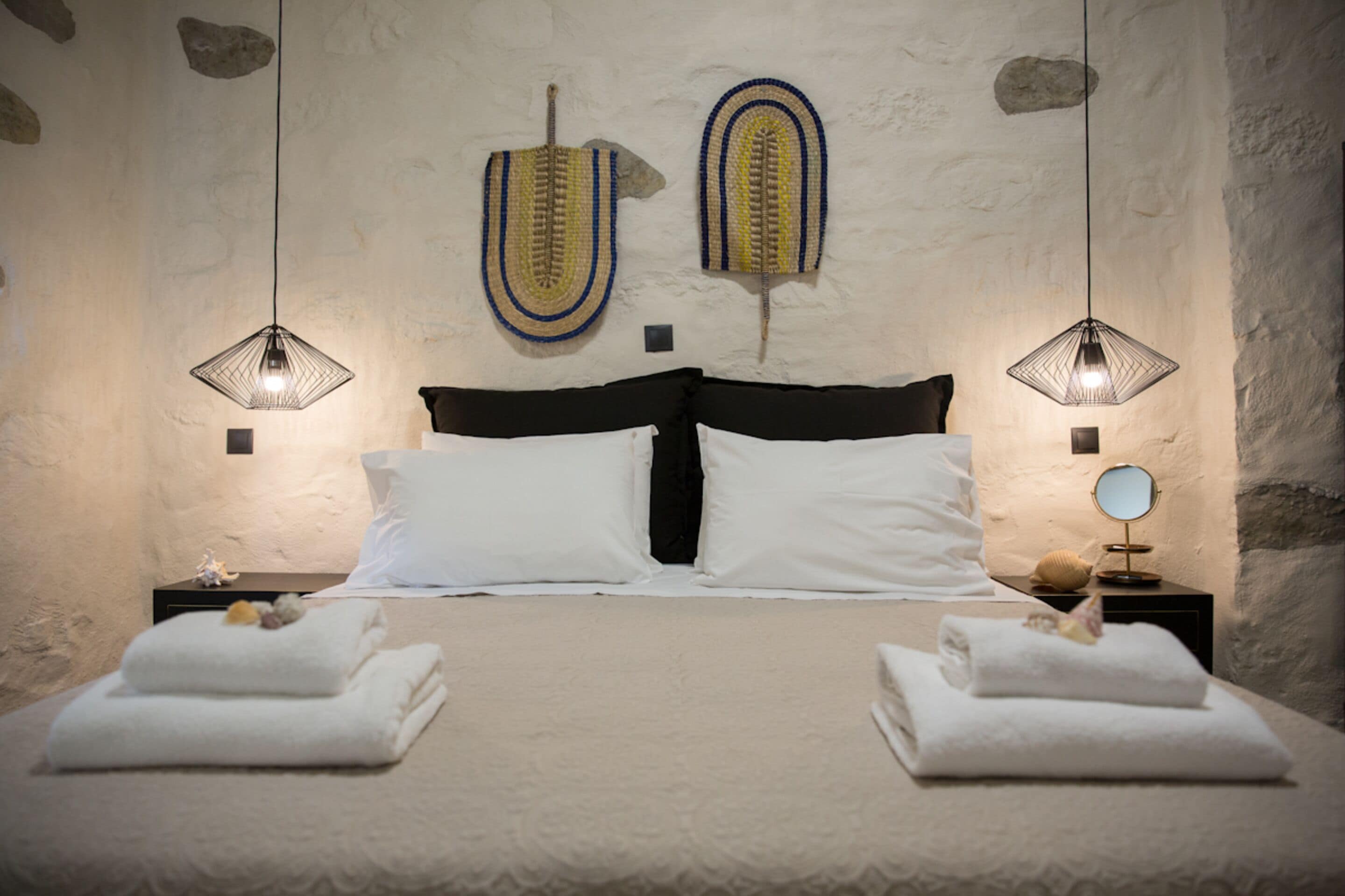 A bed with white linens, two decorative wall hangings, and two bedside lamps.