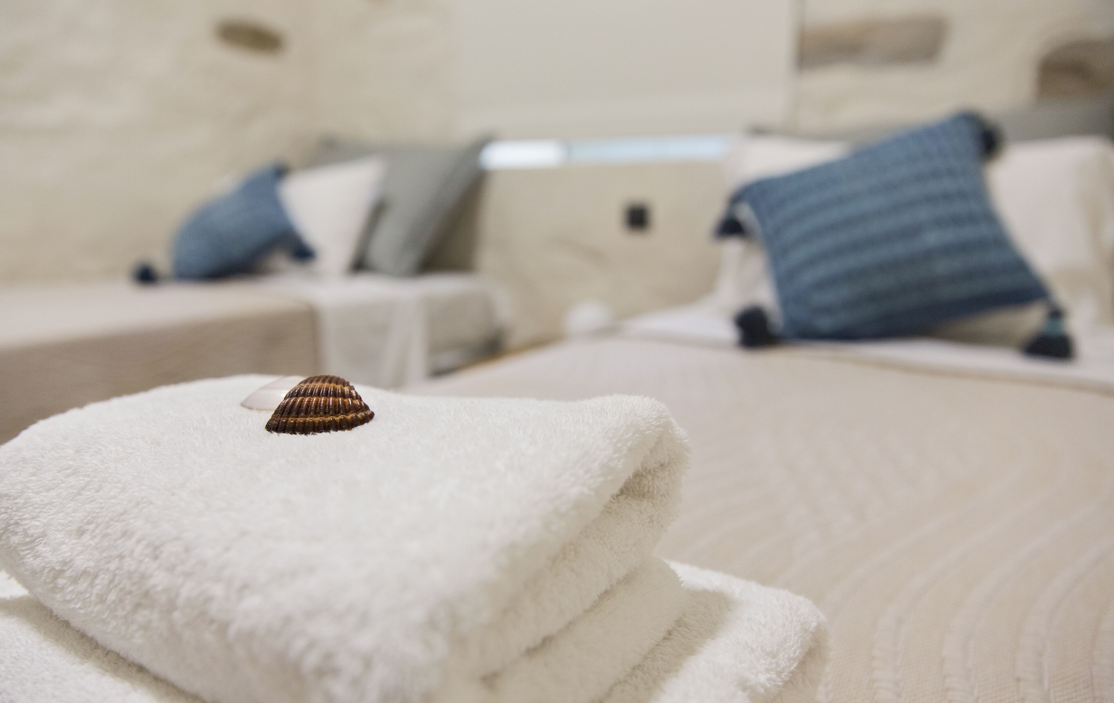 A neatly folded white towel with a seashell on top, placed on a bed with a textured white cover.