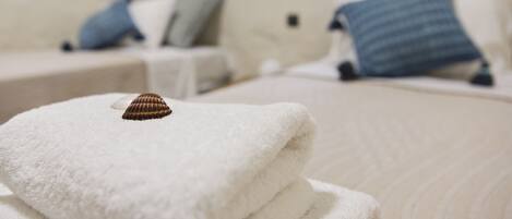 A neatly folded white towel with a seashell on top, placed on a bed with a textured white cover.