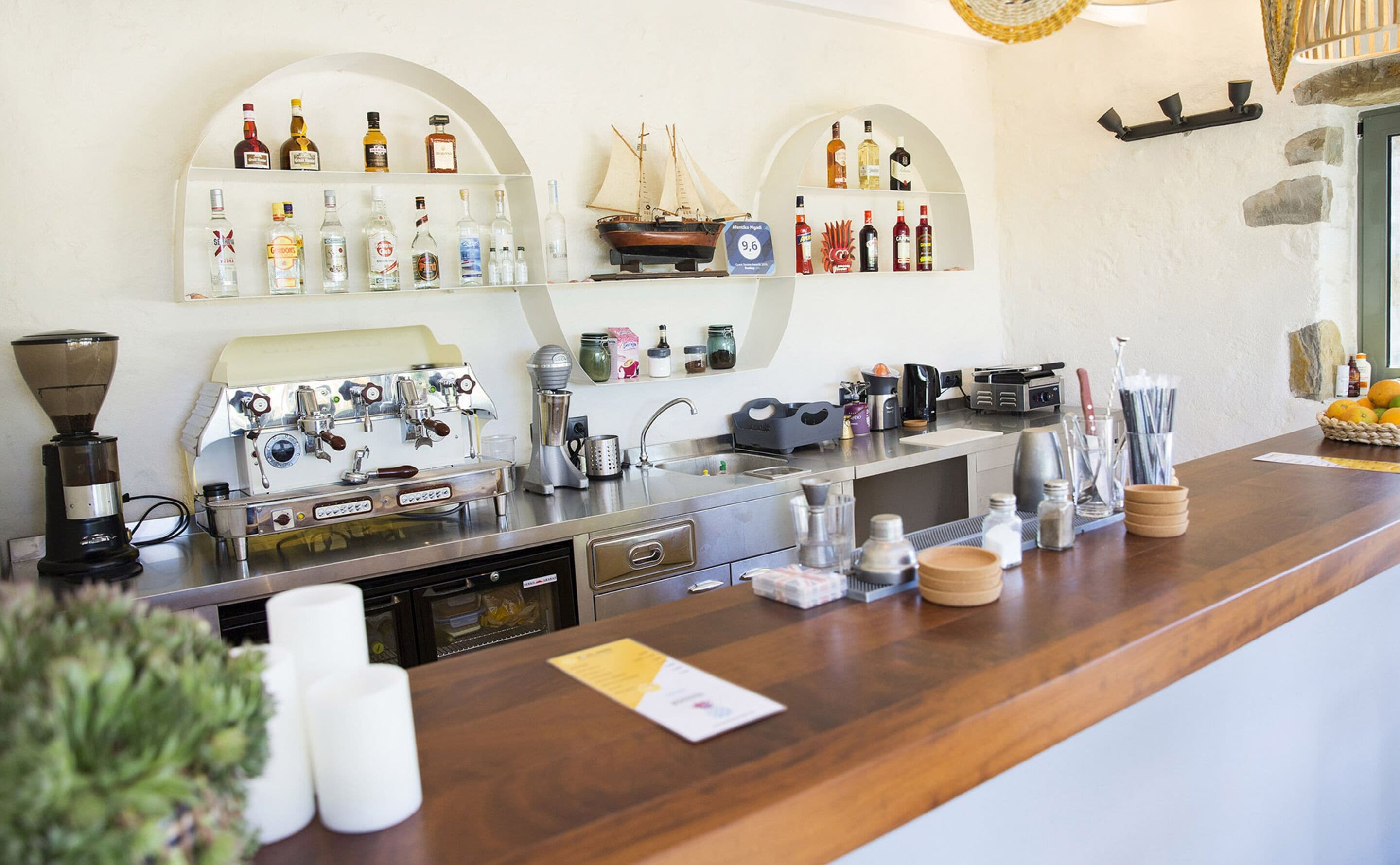 Zona de bar con máquinas de espresso, estantes de licores y un modelo de barco.