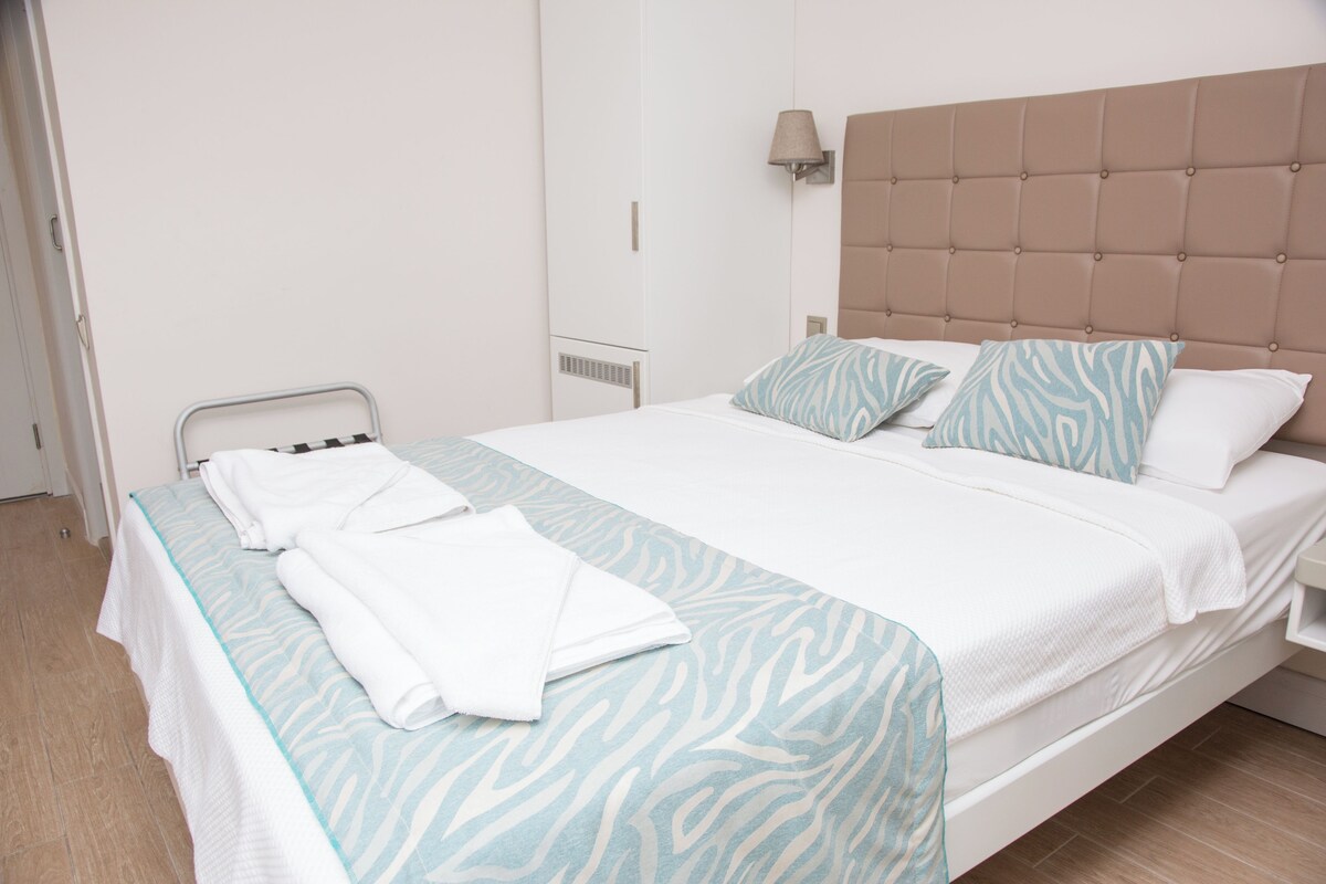 A neatly made bed with a zebra-patterned bedspread and pillows, a bedside lamp, and a white bedside table.