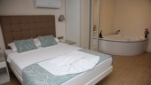 Habitación de hotel con una cama grande, una mesita de noche, aire acondicionado de pared y un baño con bañera y espejo.