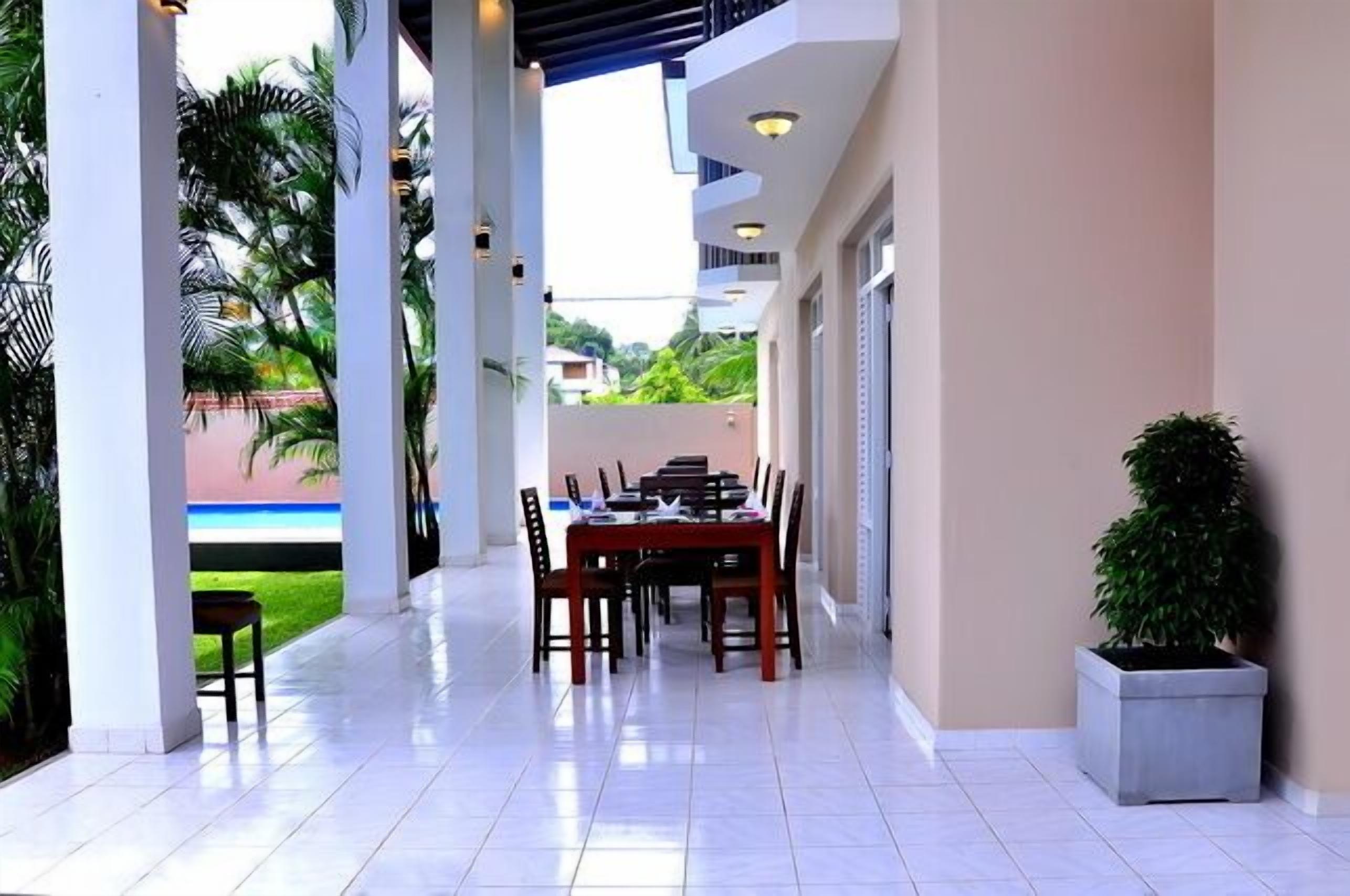 A covered outdoor dining area with a table and chairs, surrounded by white pillars and a potted plant.