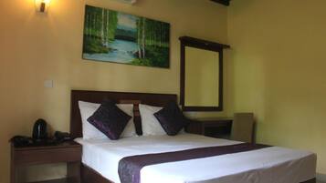 A hotel room with a bed, a nightstand, a desk, a chair, a painting, and an air conditioning unit.