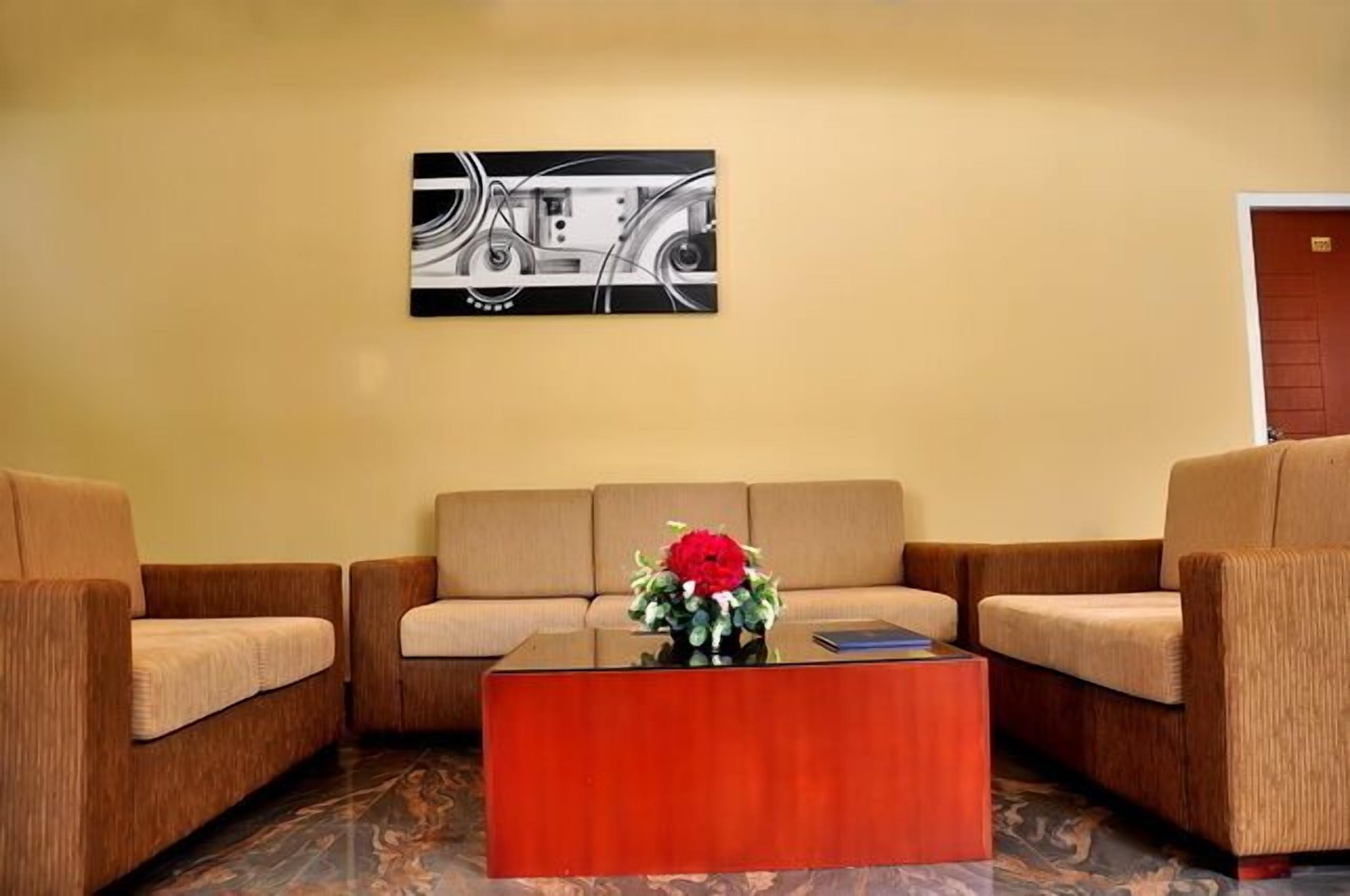 Eine Lobby mit einer beigefarbenen Sofagarnitur, einem Holztisch mit einer roten Blumenvase und einem schwarz-weißen abstrakten Gemälde an der Wand.
