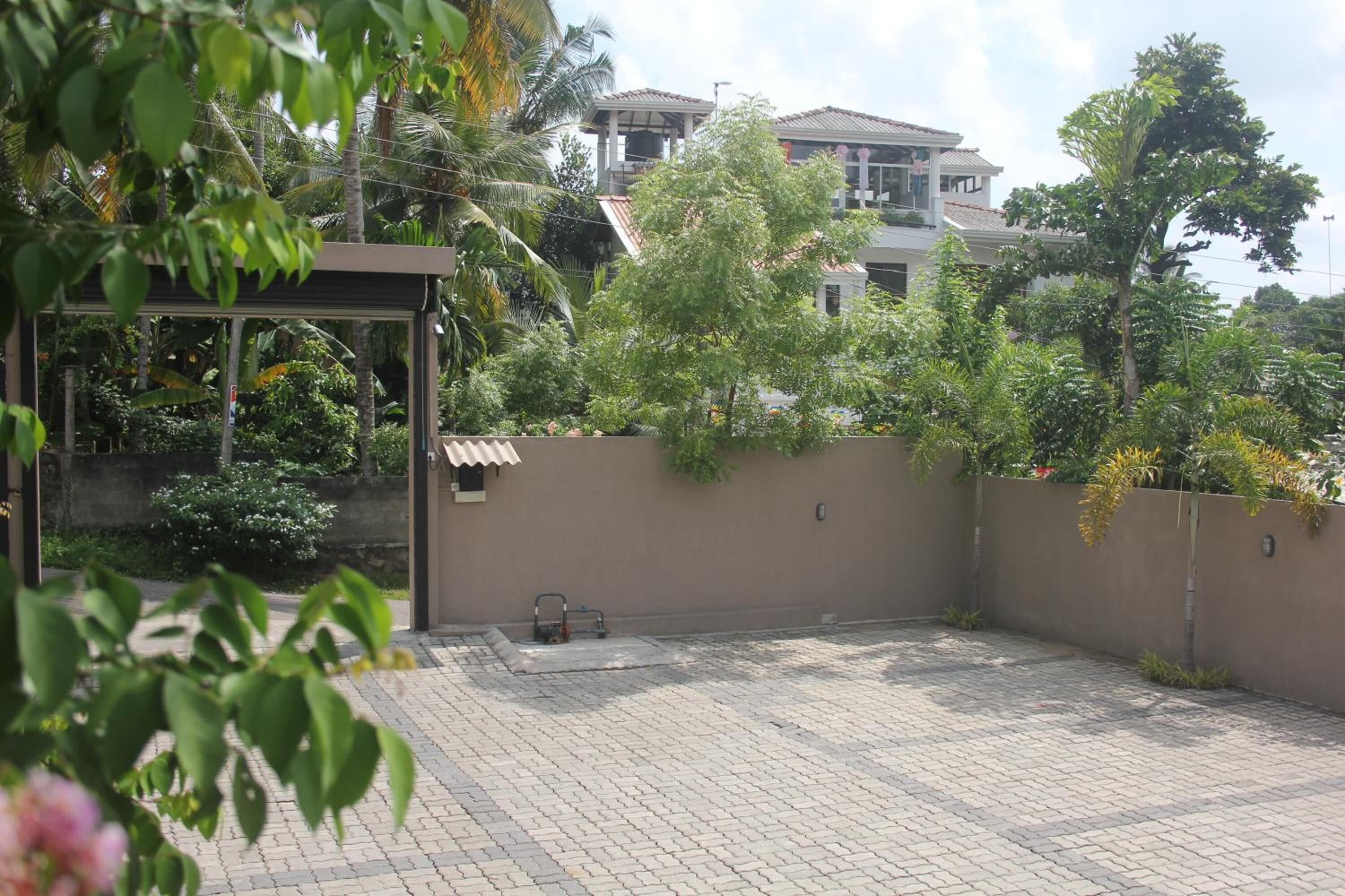 A paved courtyard with a metal gate, surrounded by lush greenery and a high wall.