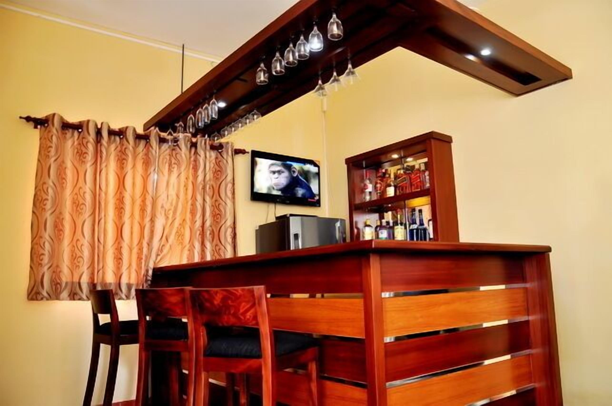 Zona de bar con mostrador de madera, televisor montado en la pared y estante con botellas.