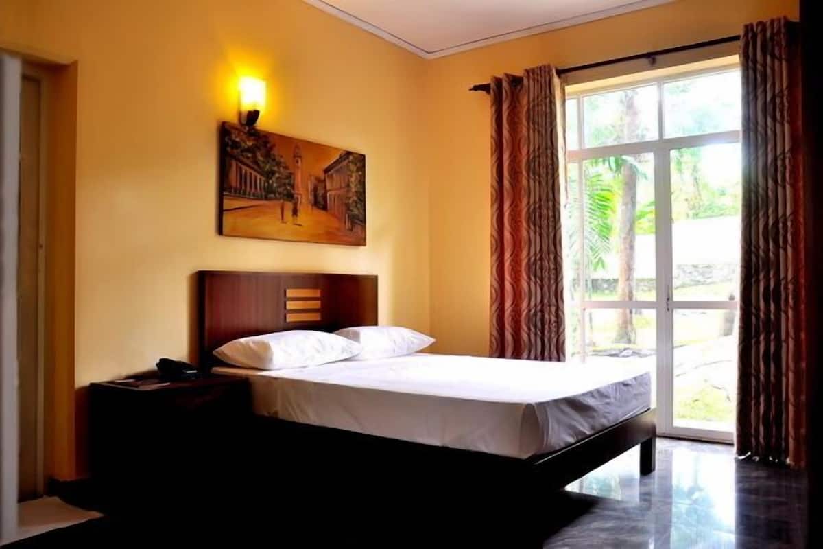 A bedroom with a bed, a nightstand, a painting on the wall, and a window with curtains.