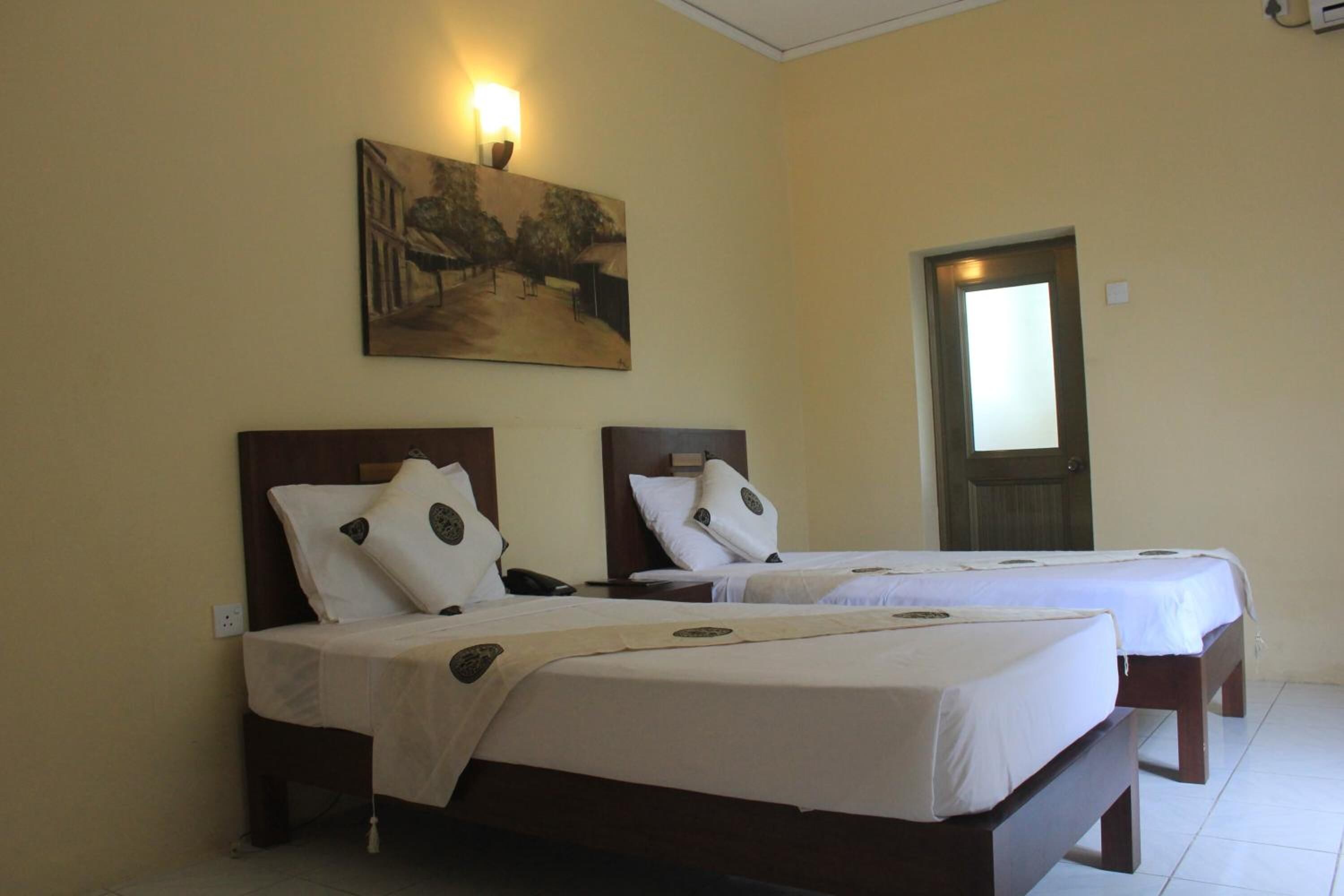 A hotel room with two single beds, a painting on the wall, and a door to the right.