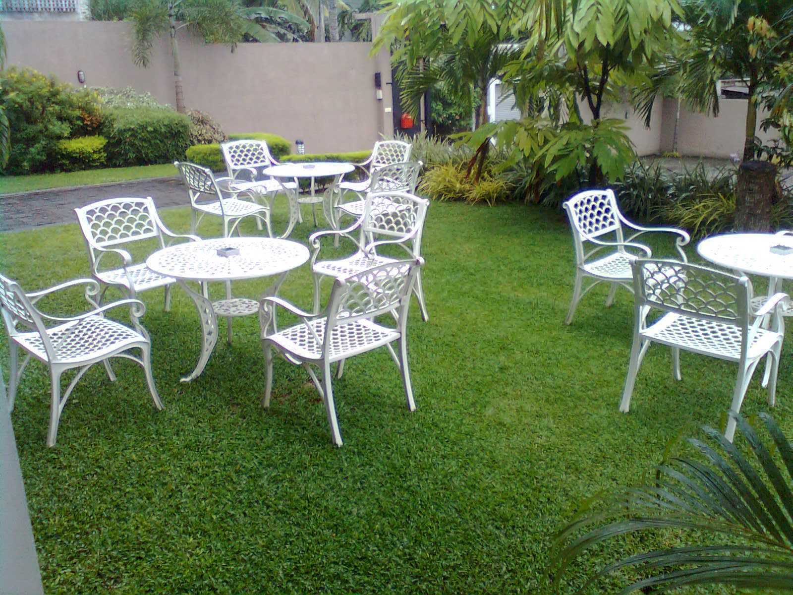 Un patio con sillas y mesas de metal blanco dispuesto sobre un césped cuidado.