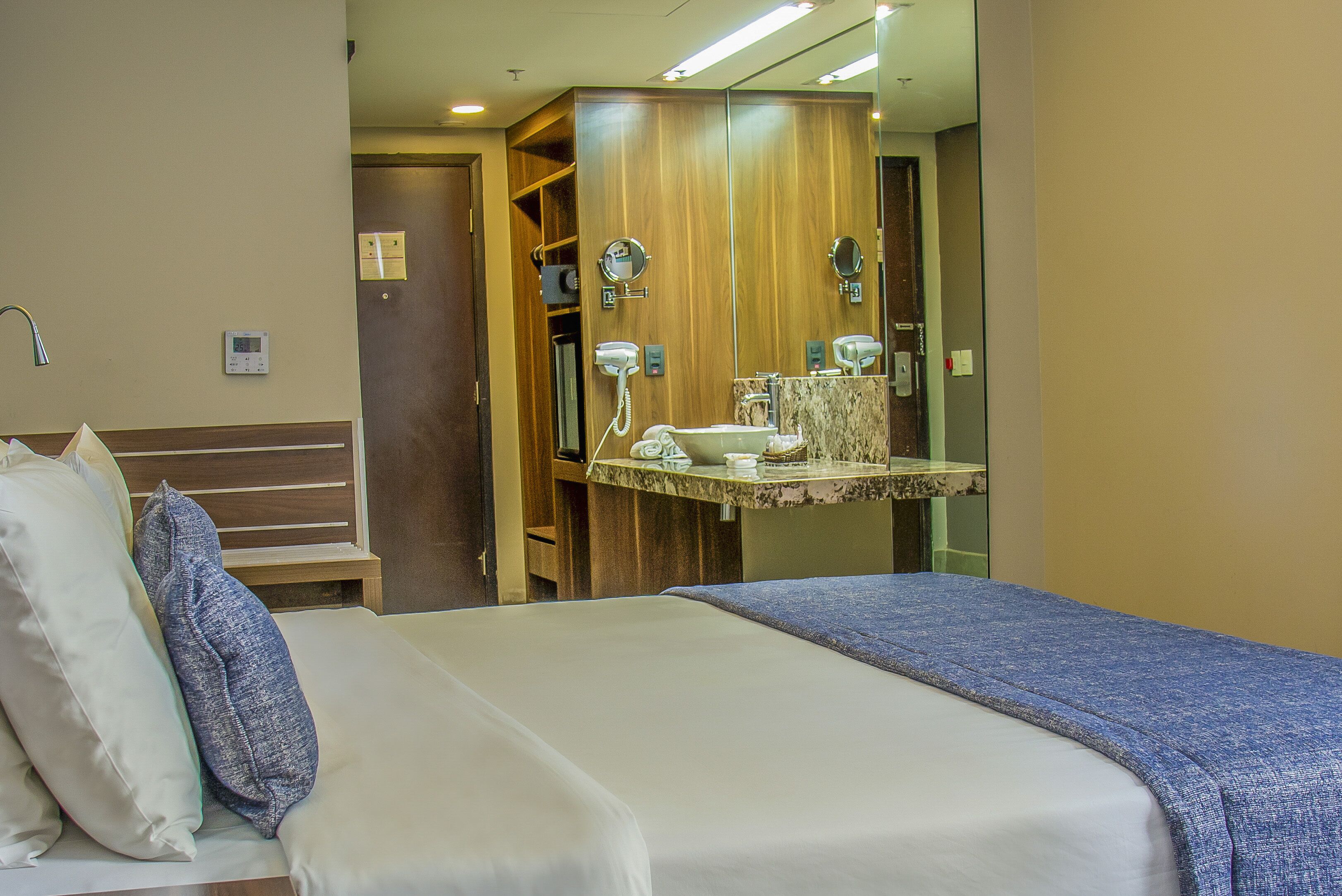 A hotel room with a bed, a bathroom with a mirror, and a wooden wardrobe.