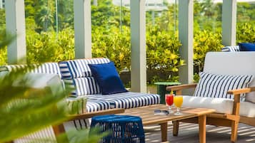 A sunlit outdoor seating area with striped cushions and a wooden table, overlooking lush greenery.
