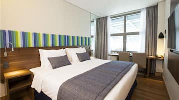 Ein modernes Hotelzimmer mit einem großen Bett, Nachttischen, einem Schreibtisch und einem Fenster mit Vorhängen.