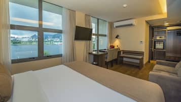 Habitación de hotel con una cama grande, un escritorio con silla, un sofá y un televisor fijado a la pared.