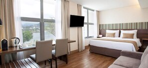 A hotel room with a bed, a desk with chairs, a television, and a view of the outdoors.