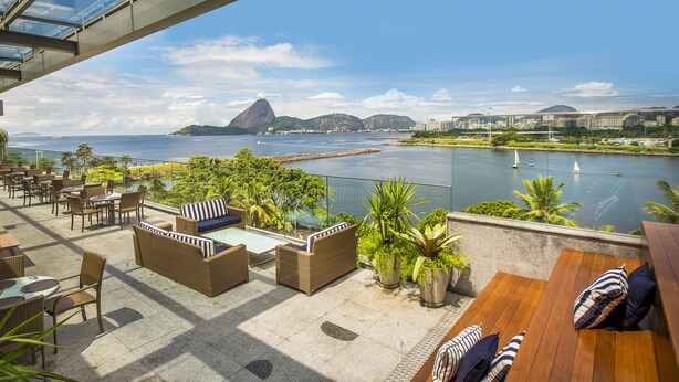 A rooftop terrace with outdoor seating, a pool, and a view of the water and mountains. -  Prodigy Santos Dumont by Wish (Rio de Janeiro)