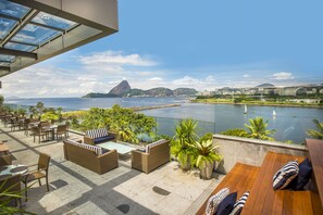 Una terraza en la azotea con mobiliario exterior, una piscina y vistas al agua y a las montañas.