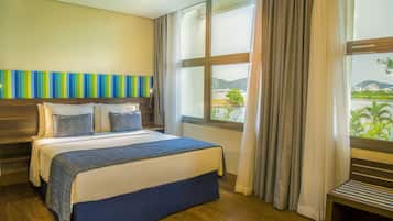 Una habitación de hotel con una cama grande, un cabecero de madera, vista a un paisaje urbano a través de una ventana y un adorno en la pared con rayas.