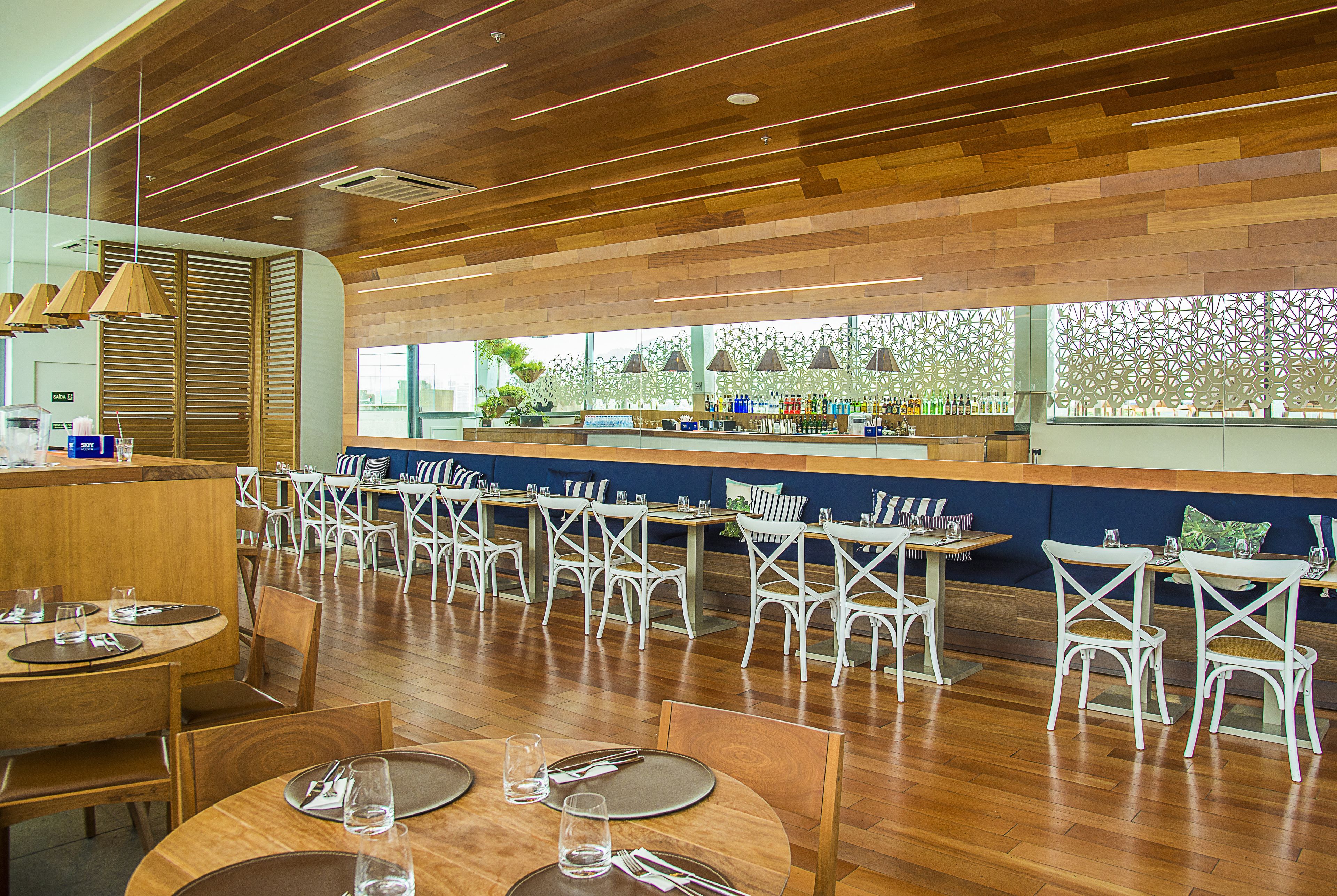 Un restaurante con suelo de madera, sillas blancas y una zona de bar.