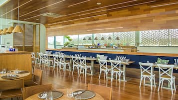 Un restaurante con suelo de madera, sillas blancas y una zona de bar.