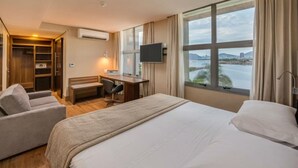 A hotel room with a large bed, a desk, a chair, a TV, and a view of a body of water. -  Prodigy Santos Dumont by Wish (Rio de Janeiro)