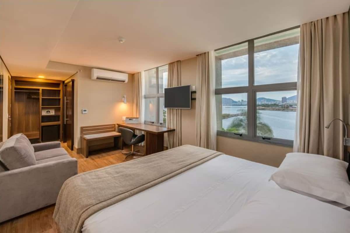 Habitación de hotel con una cama grande, un escritorio, una silla, un televisor y vista a un cuerpo de agua.