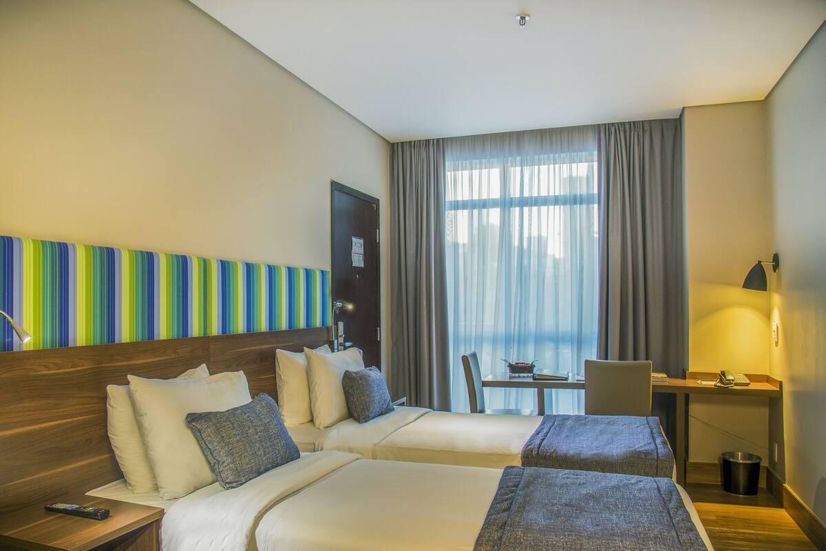 Habitación de hotel con dos camas, un escritorio, una silla y una ventana con cortinas.