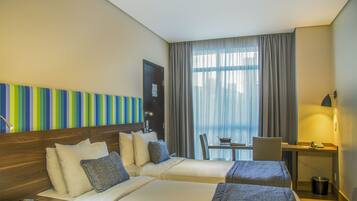 A hotel room with two beds, a desk, a chair, and a window with curtains.