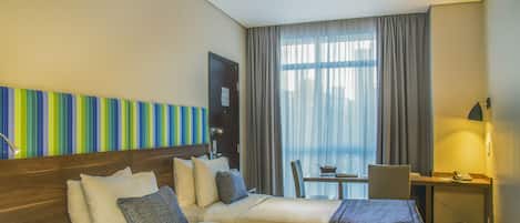 Habitación de hotel con dos camas, un escritorio, una silla y una ventana con cortinas.