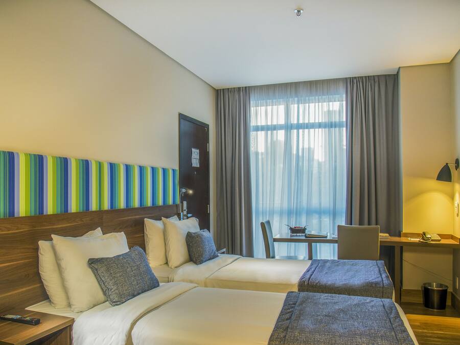 A hotel room with two beds, a desk, a chair, and a window with curtains.