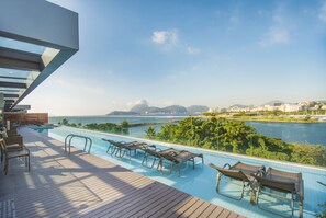 A poolside area with lounge chairs and a view of a body of water and distant cityscape.