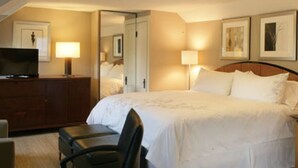 A hotel room with a bed, a desk with a television, a chair, and two bedside lamps. - Mooncussers Tavern and Inn (Harwich Port)