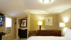 A hotel room with a large bed, a desk with a computer, a TV, and a bathroom with a mirror and sink. - Mooncussers Tavern and Inn (Harwich Port)