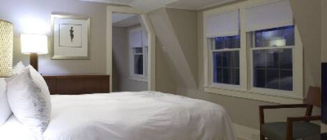 A bedroom with a bed, a chair, a lamp, and a window.