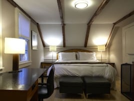 Quarto com cama, duas mesas de cabeceira com abajures, escrivaninha e uma cadeira.