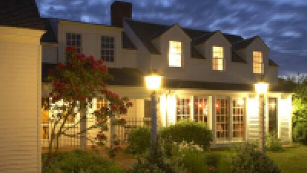A two-story house with a well-lit front porch and a garden. - Mooncussers Tavern and Inn (Harwich Port)
