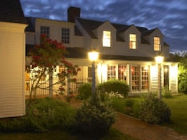 Uma casa de dois andares com varanda iluminada e jardim.