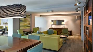A modern hotel lobby with a wooden reception desk, green sofas, and a large abstract painting on the wall.