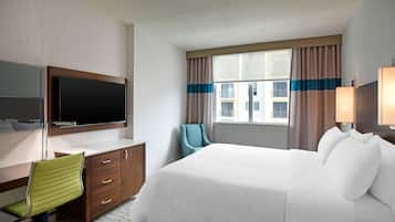 Ein Hotelzimmer mit Bett, Schreibtisch mit Stuhl, Fernseher und einem Fenster mit Vorhängen.