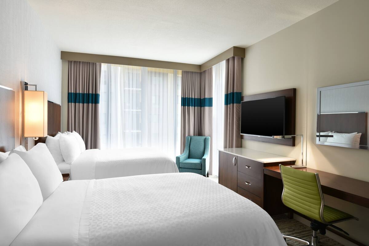A hotel room with two beds, a desk, a television, and a chair.