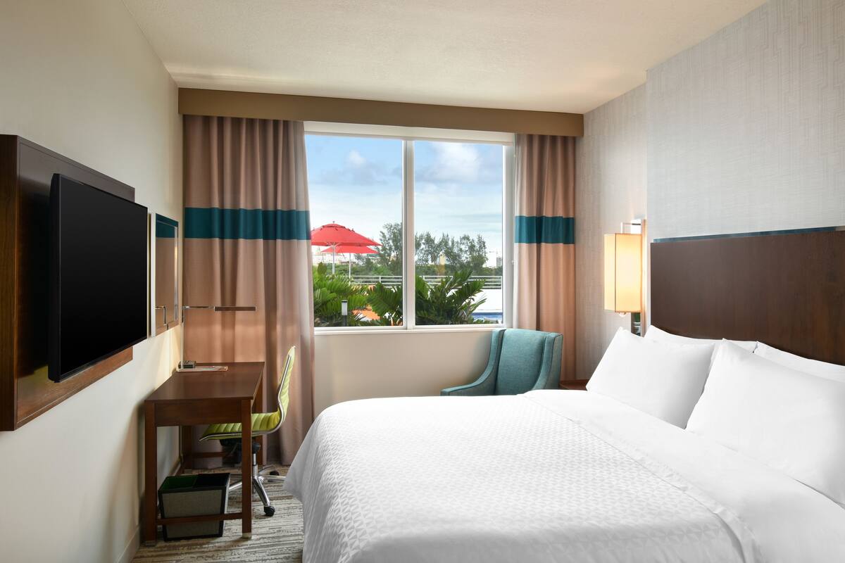 A hotel room with a bed, a desk, a chair, a television, and a window with curtains.