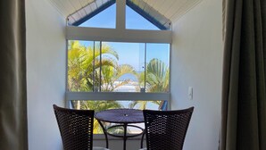 A room with a large window overlooking a beach and palm trees. There is a wicker table and two chairs in front of the window. - Pousada Kaliman Ubatuba (Ubatuba)