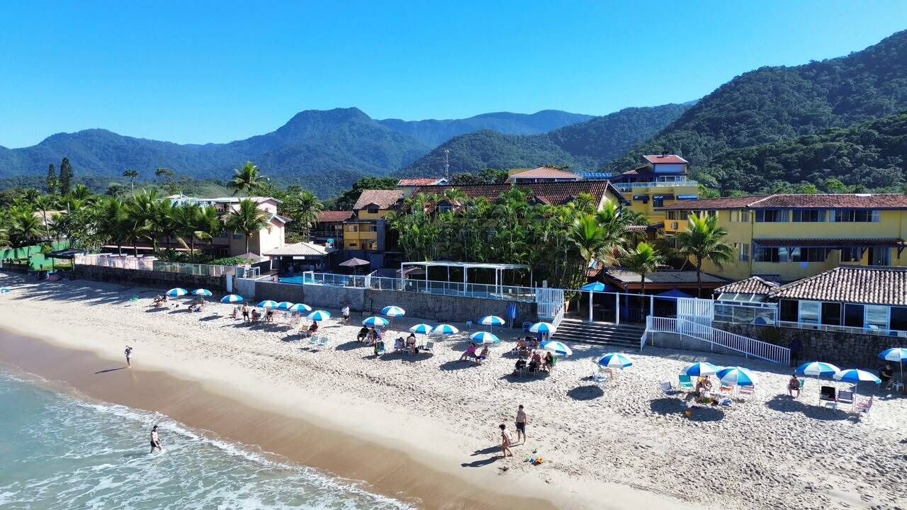 A beach with umbrellas, people, and buildings in the background.