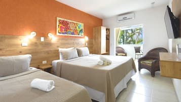 A hotel room with two beds, a wooden headboard, a colorful wall art, a window with a view of palm trees, a TV, and a wicker chair.