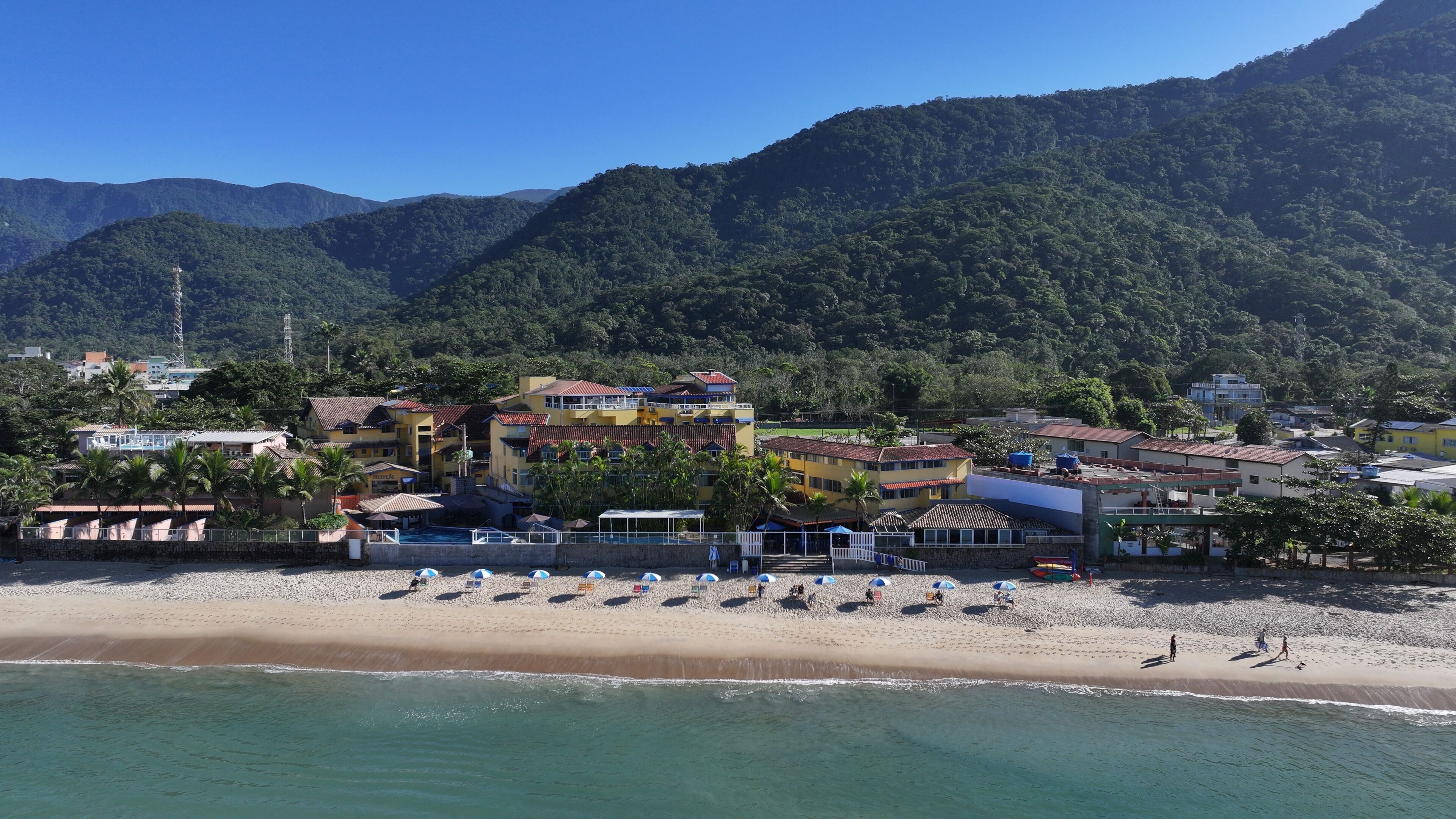 Un resort costero con alojamiento frente a la playa, piscina y vistas a las montañas circundantes.