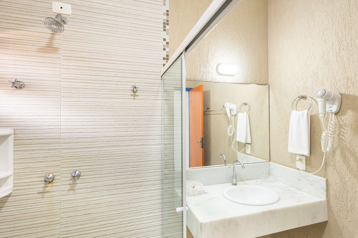 A modern bathroom with a glass-enclosed shower, a sink with a mirror, and a hairdryer mounted on the wall.