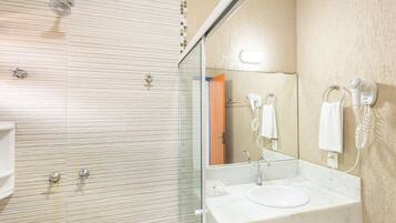 Une salle de bain moderne dotée d’une douche à parois de verre, d’un lavabo avec un miroir et d’un sèche-cheveux fixé au mur.
